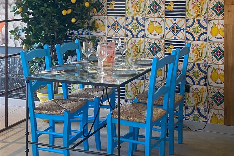 Mesa de hierro y sillas azules frente a la pared de azulejos con limones