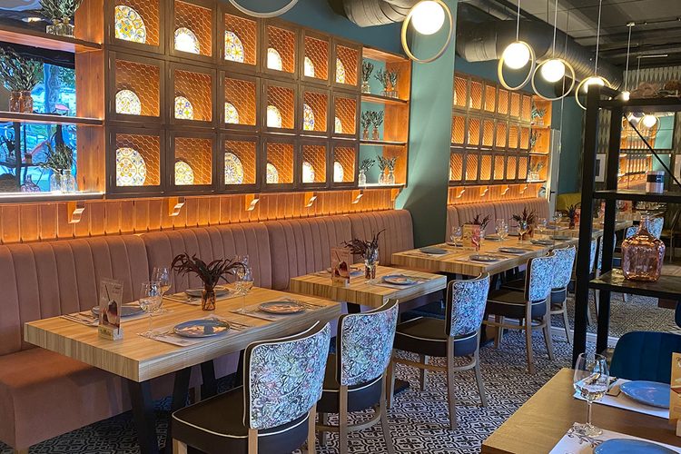 Banco corrido y mesas puestas bajo una estanteria de azulejos italianos en el restaurante de Andorra