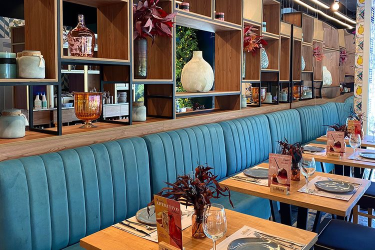 Banco corrido azul y mesas de madera preparadas para cenar en el restaurante La Famiglia de Andorra